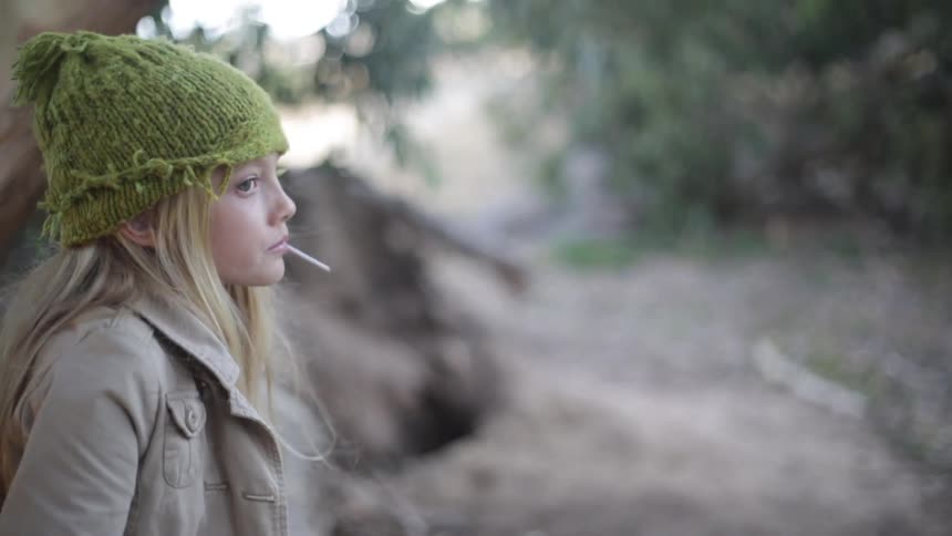 A girl sucking a lollipop looks around while standing in the wilderness