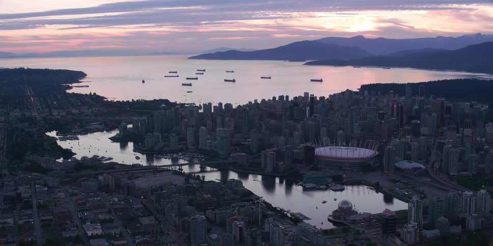 Channel water reflects nearby buildings as sun shines from mountains on the horizon