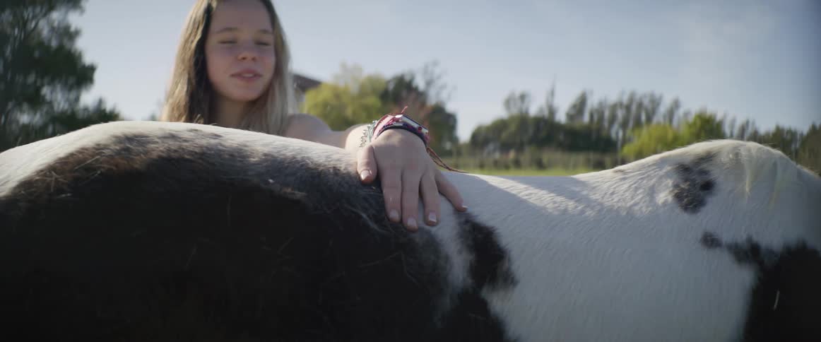 Girl stands petting horse in field with house in the background