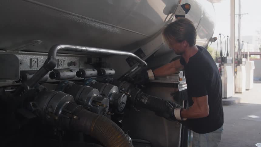 A man wearing gloves is attaching a hose to a truck with a large tank on it