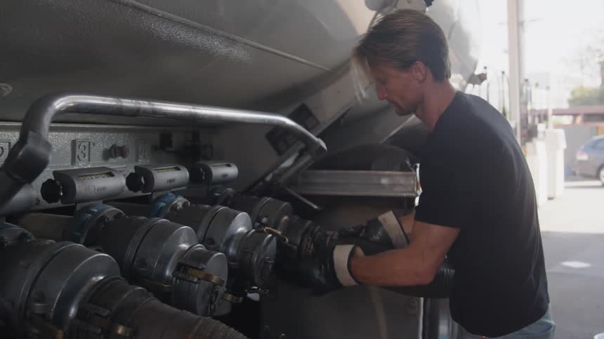 Man connects hose to tanker truck and maneuvers it toward underground tank