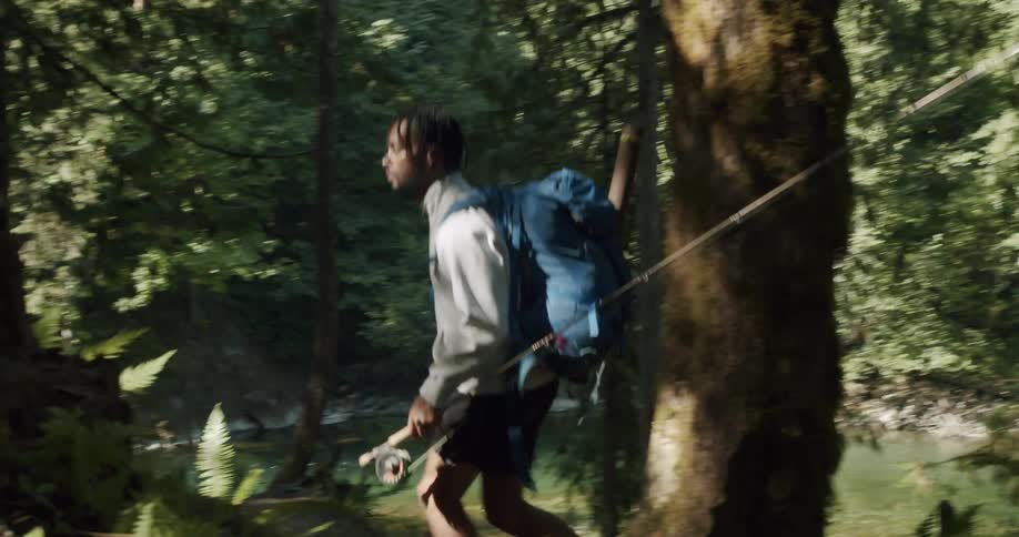 A man carrying a fishing pole hiking in the forest near a lake