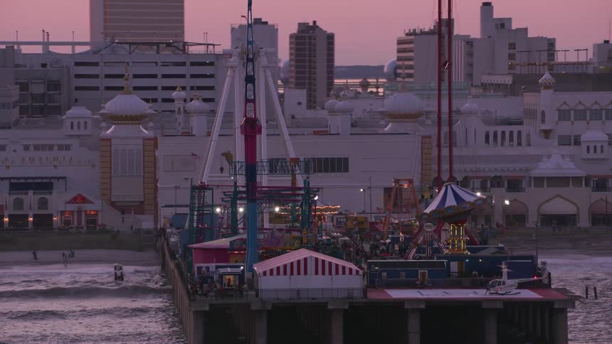 Carnival rides on an ocean pier in a big coastal city at sunset