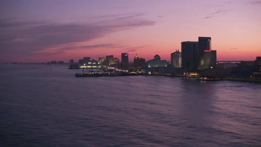 Lights shine on pier and city buildings under red sky