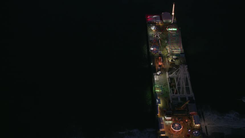 Aerial view of a lit up pier with rides at night at the beach