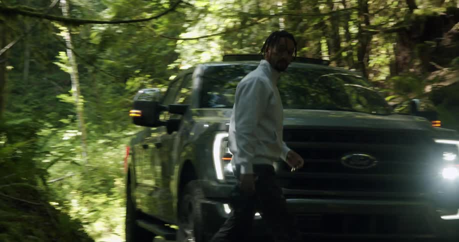 A man walks around his truck with a camera in the woods