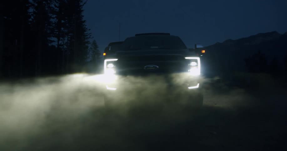 A pickup truck drives through a cloud of dirt in the forest