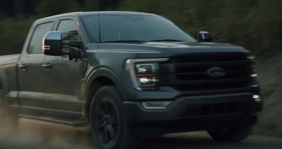 A black pickup truck travels on a dirt road and leaves a trail of smoke behind it