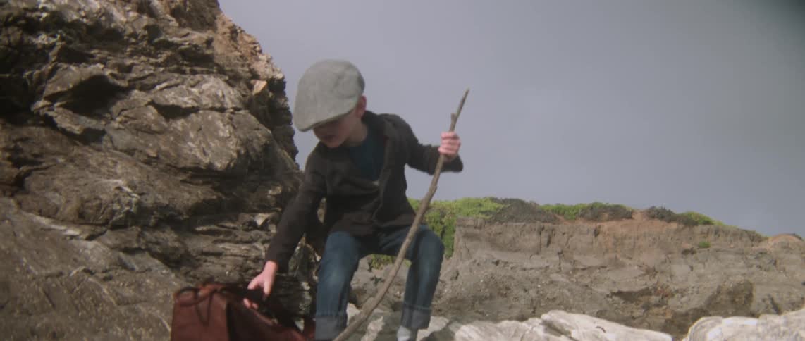 A boy wearing a hat sets his backpack down and unbuttons his jacket
