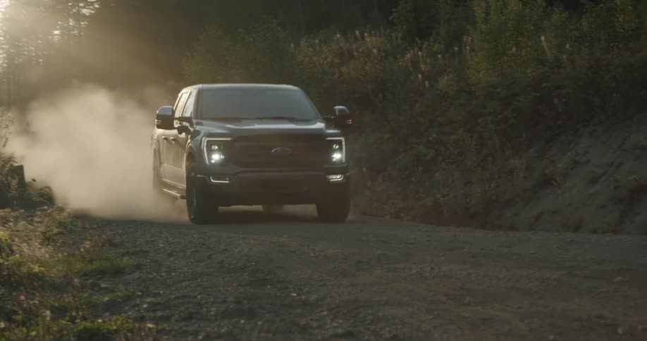A black pickup truck travels on a dirt road and leaves a trail of smoke behind it
