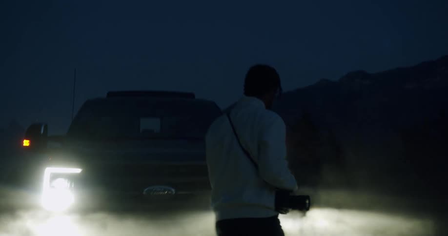A person is walking near a car during the night time