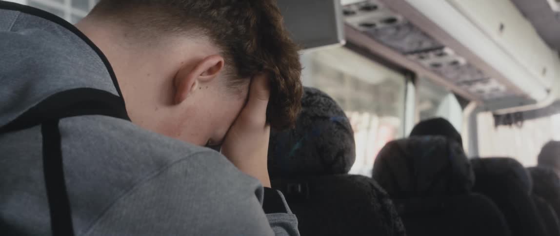 Man sits on moving bus with his bowed head resting on his hand