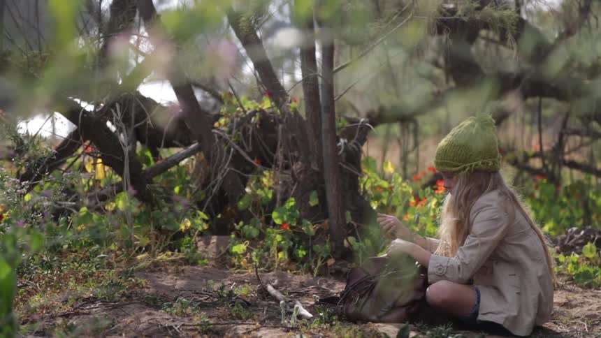 Girl sits on the ground outside while holding  and fidgeting with a necklace