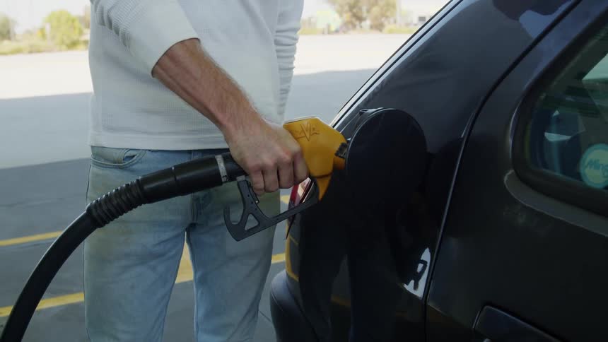 A man puts a gas pump into an automobile as he fills it with gas