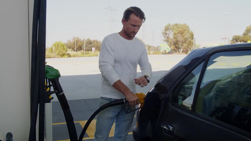 A man puts a gas pump into an automobile as he fills it with gas