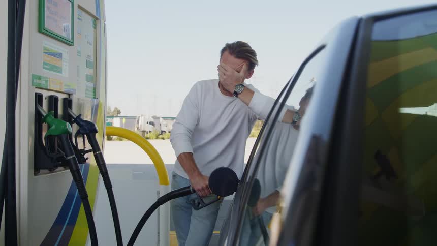 Man sleepily wipes his eyes as he stands near car pumping gas