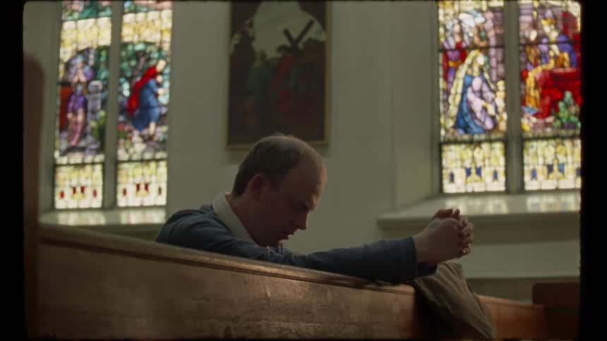 Man sits in church pew praying with his head bowed