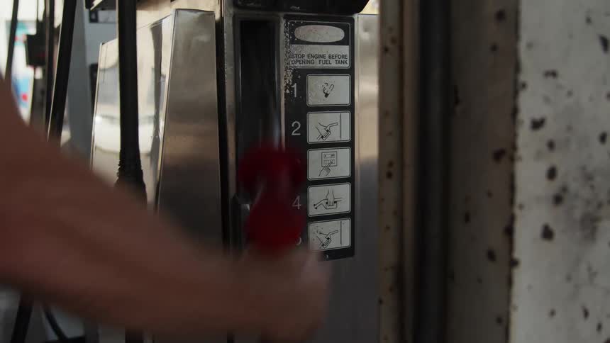 A man lifts the nozzle at a gas station pump on a sunny day