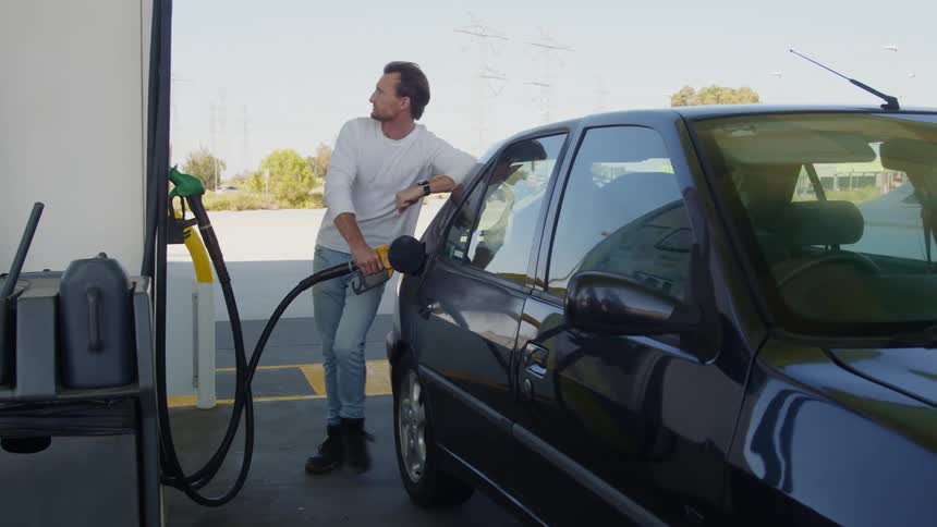 A man is standing outside putting gas in his car at a gas station