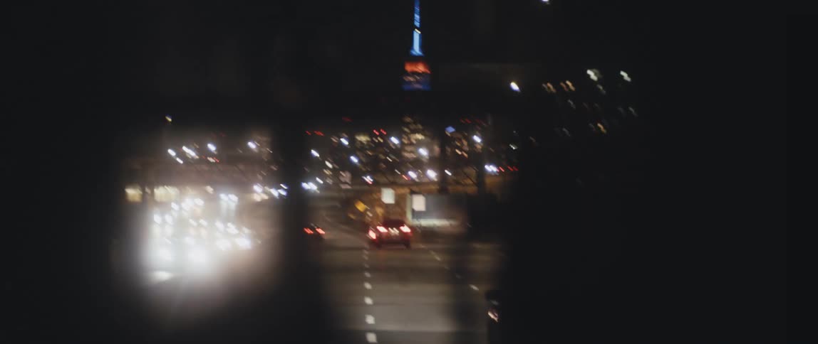 Traffic flows along controlled access highway near brightly lit buildings at night