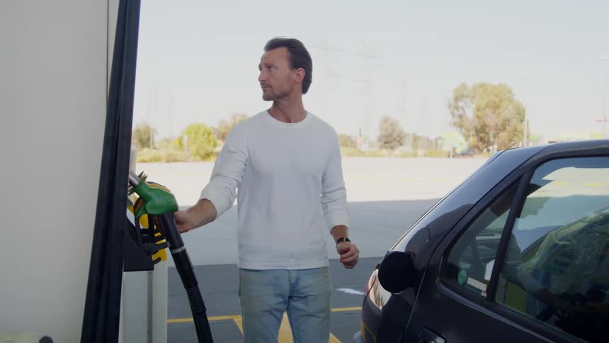 A man takes the gas cap off his car and puts in a gas pump hose to fill it with gas