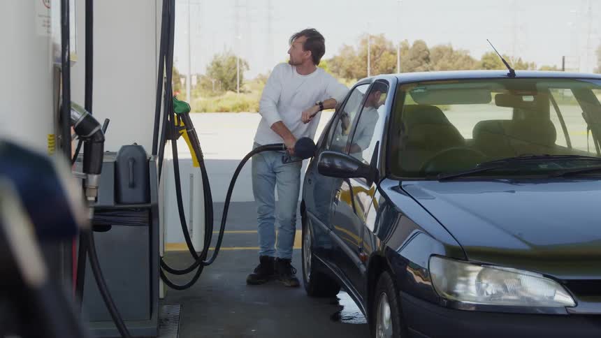 A man puts a gas pump into an automobile as he fills it with gas