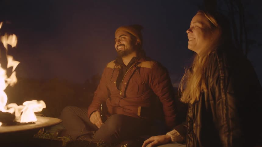 A man and a woman sitting near a campfire smiling