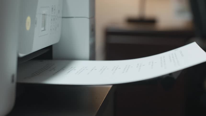 A sheet of paper comes out of a printer and someone takes it