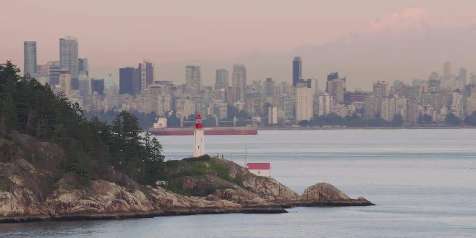 A lighthouse overlooks the water as ships sail and the city skyline is in the distance
