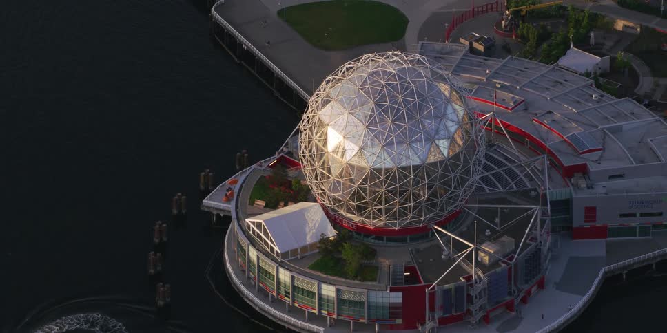 Circular building with sphere on top sits over water at edge of park under use by several people