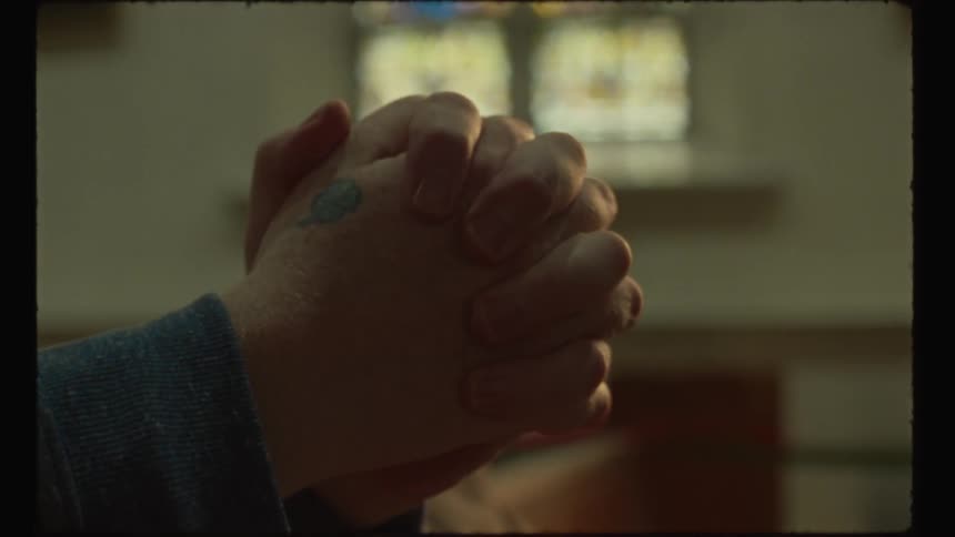 A person has their hands clasped together in prayer while they are located within a church