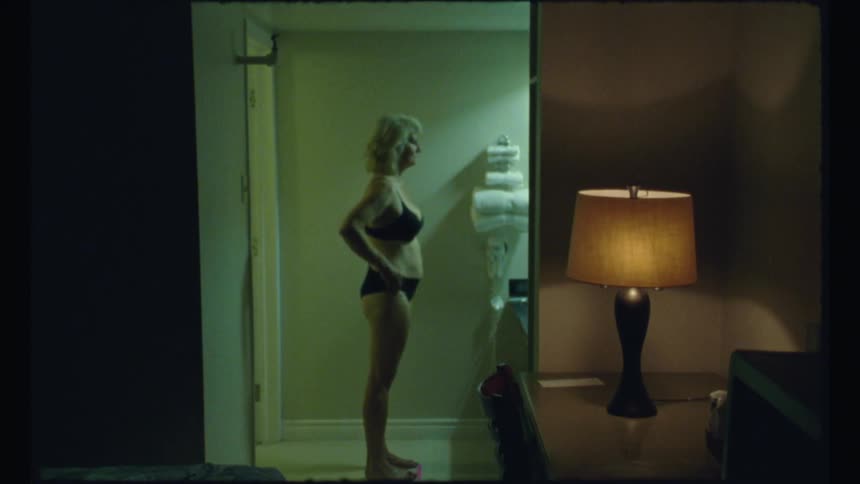 A woman stands in a hotel bathroom in her underwear and looks at herself in the mirror