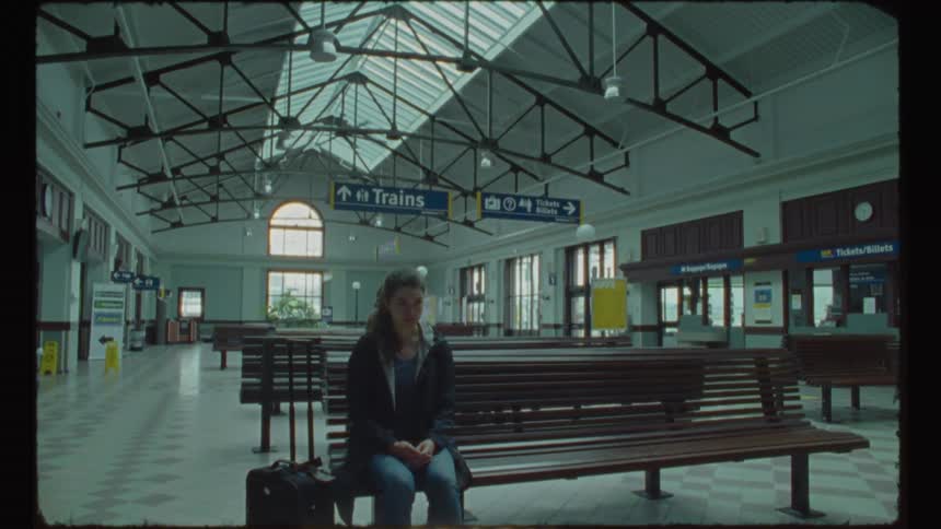 Woman sits waiting on bench in empty train station
