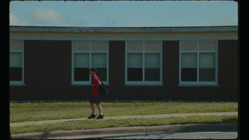 A boy wearing a backpack walks past a school building on a sunny day