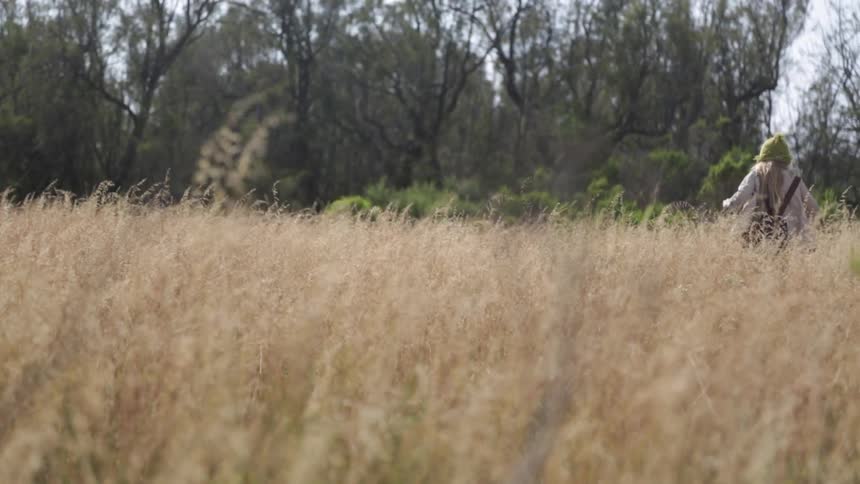 A girl holding a stick is walking through a field