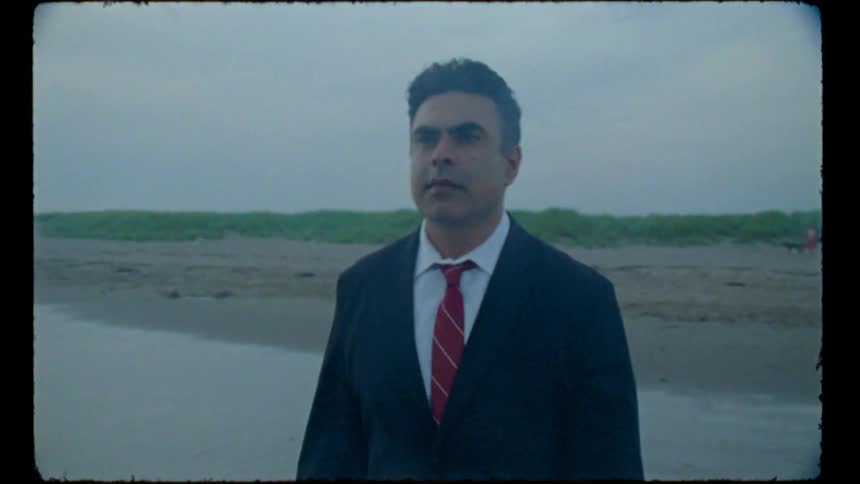 A man in a suit walks on the beach