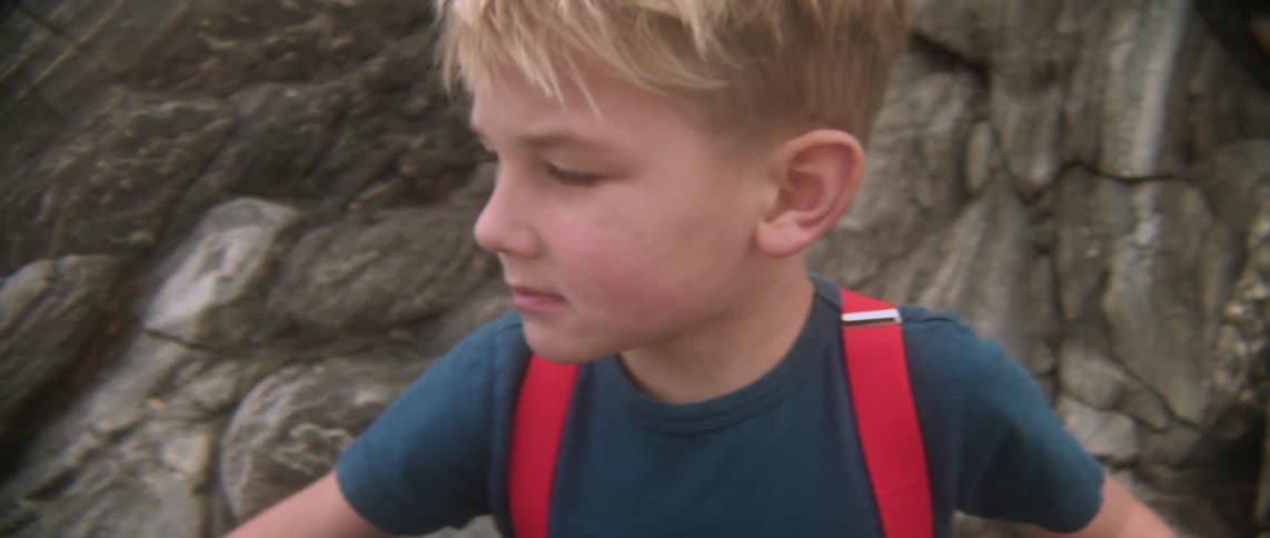 A boy is standing near some rocks