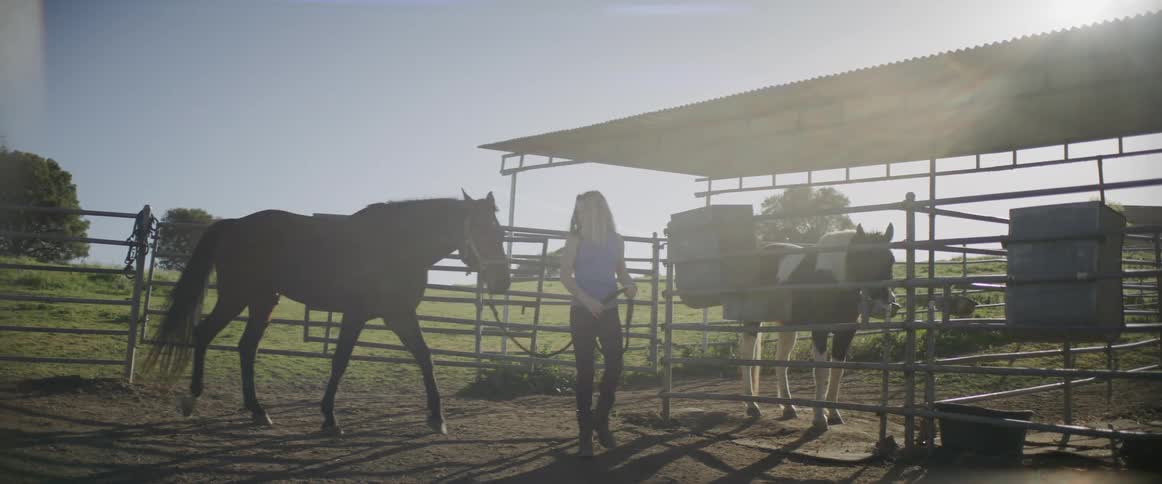 A woman is walking around a ranch with a horse