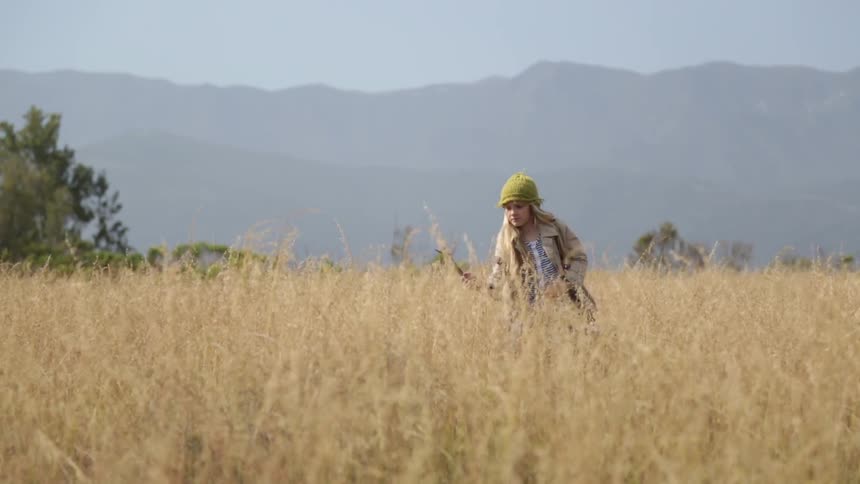 A girl holding a stick is walking in tall yellow grass