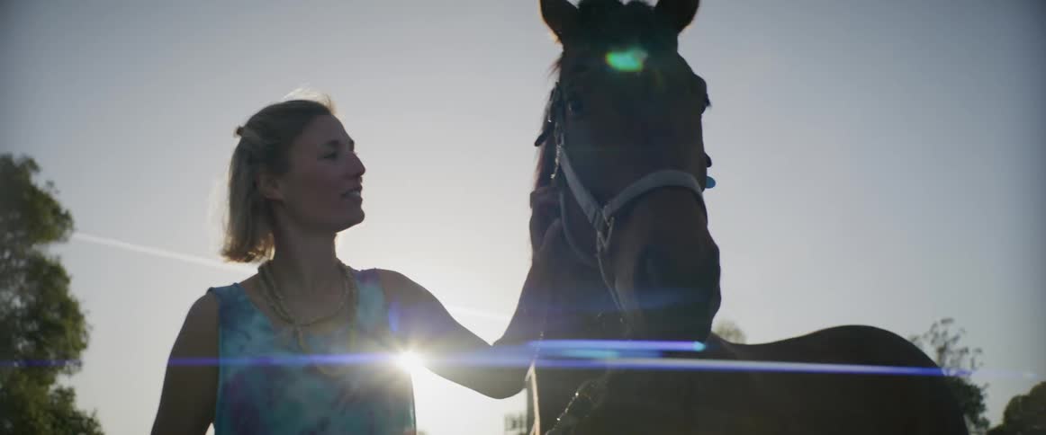 A woman is petting a horse in a rural area at dusk