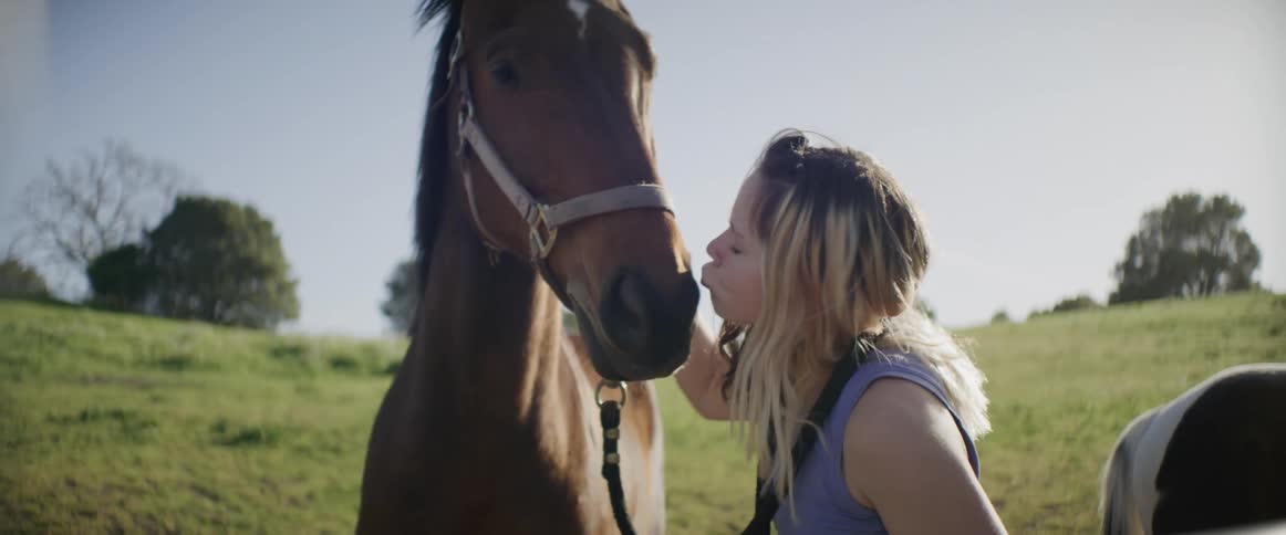 A woman is petting her horse and gives it a kiss
