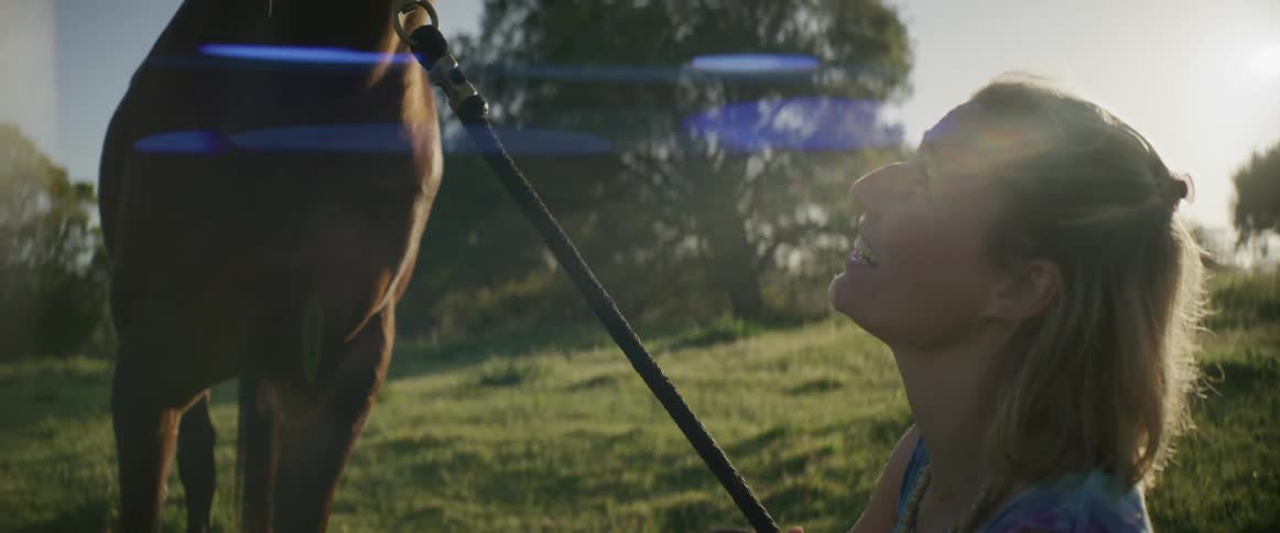 Woman with brown hair looks up at brown horse in the grassy field