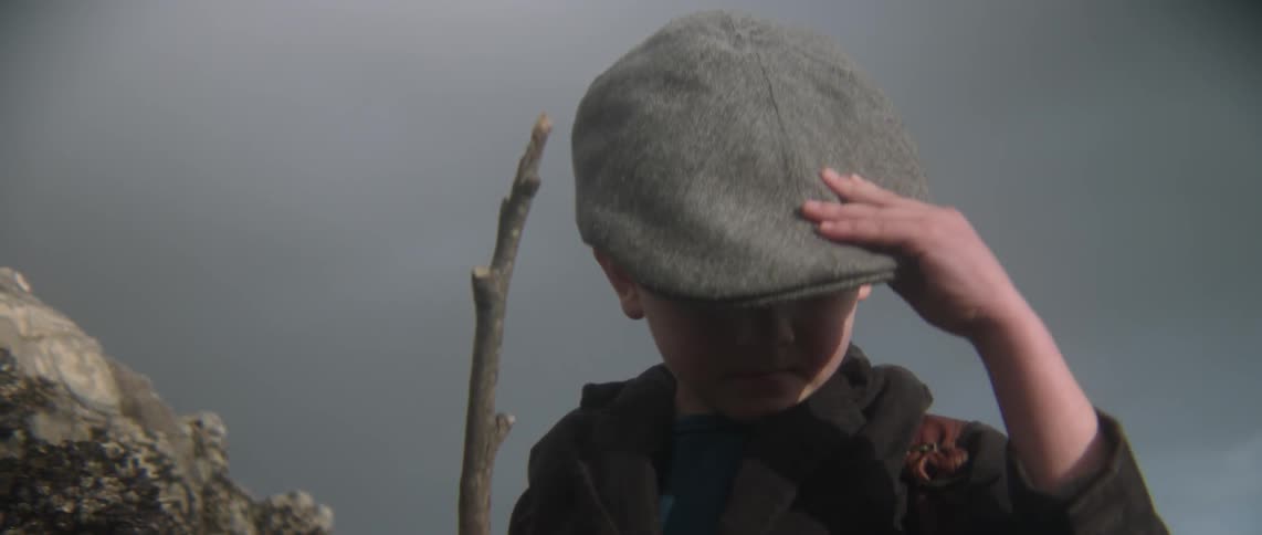 A child is holding a stick then puts on his hat
