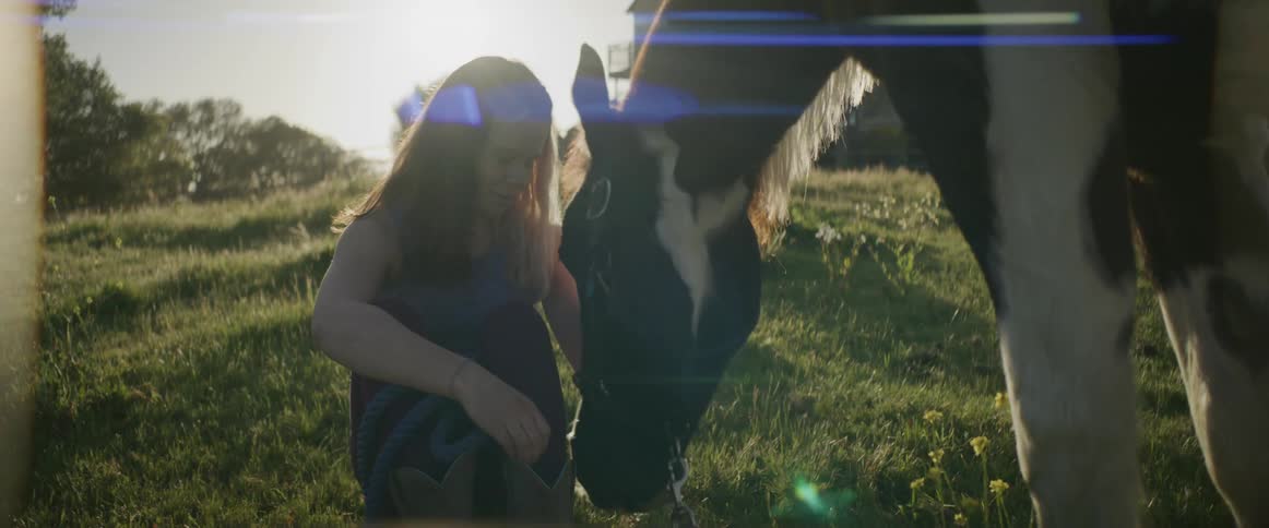 A girl sits as the horse is grazing