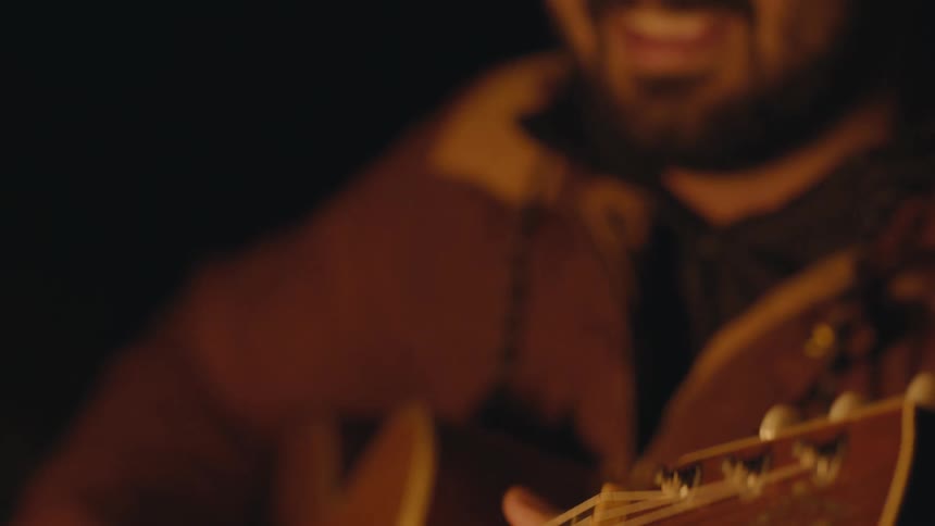 Young man plays guitar next to campfire at night