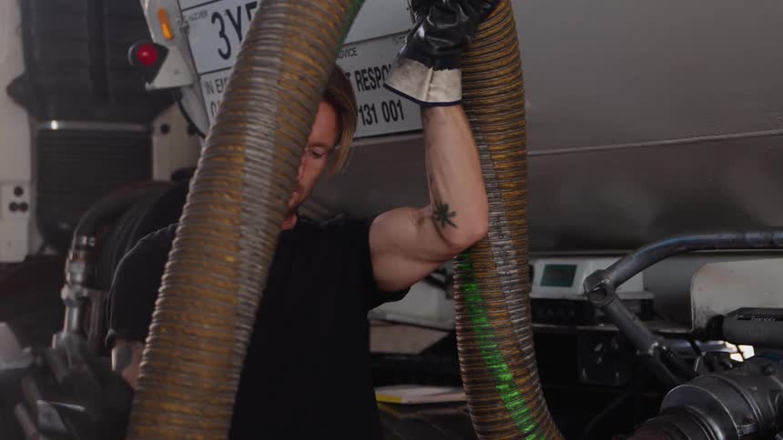 A man lifts the hose to deliver gas at a station