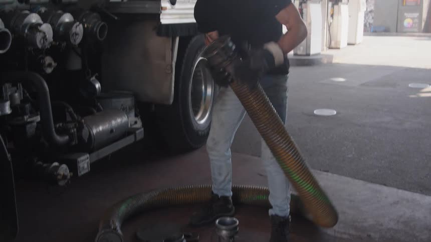 A man removes the hose from the underground tank at a gas station after refilling