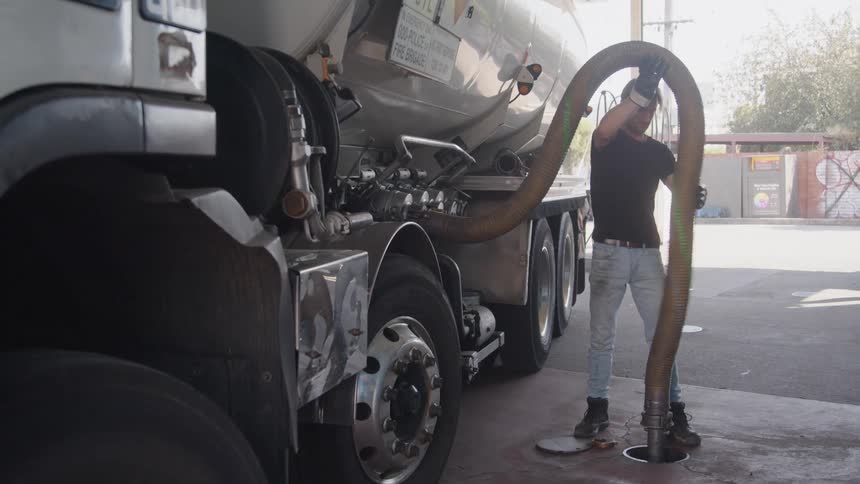 A man is pumping gas into the station from his delivery truck