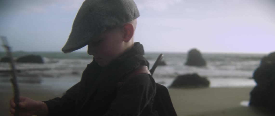 A boy is standing on the sand of a beach