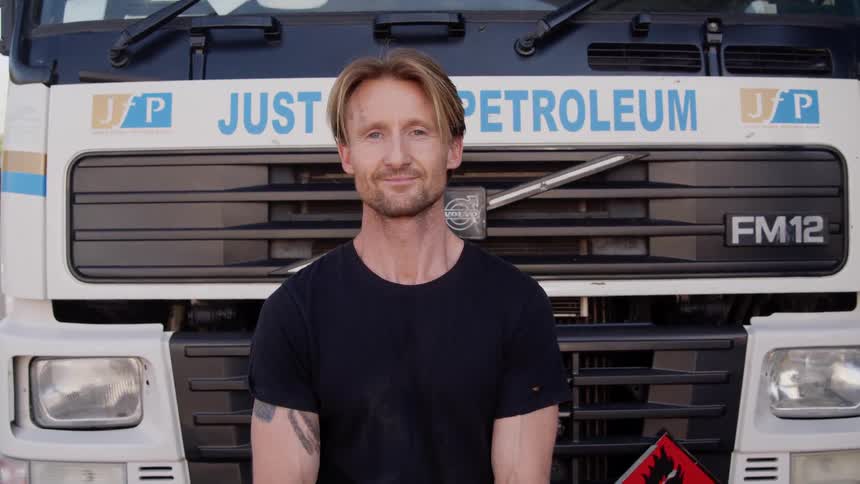 A man is standing in front of his vehicle and smiling